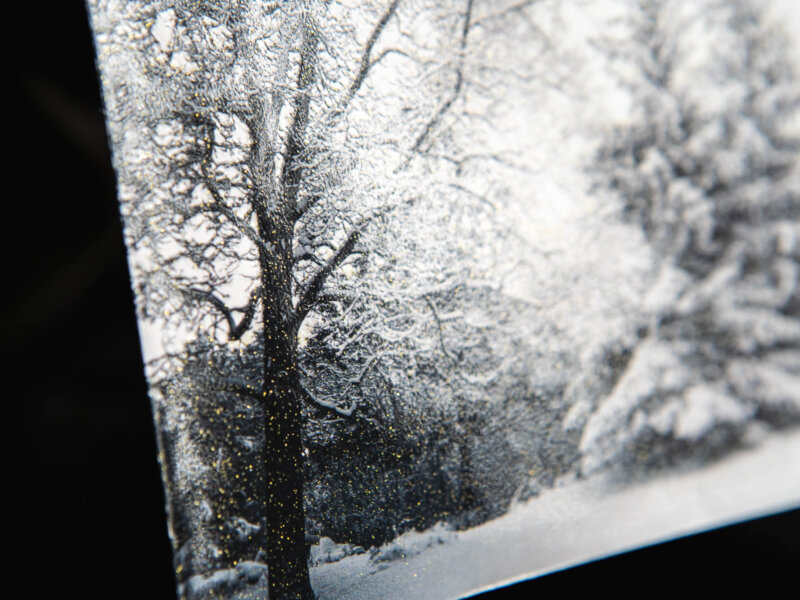 Up close detail of golden sprinkles on an envelope with a picture of snowy trees as the background