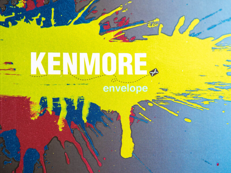 Kenmore Envelope logo with a splattered yellow, blue and red paint background
