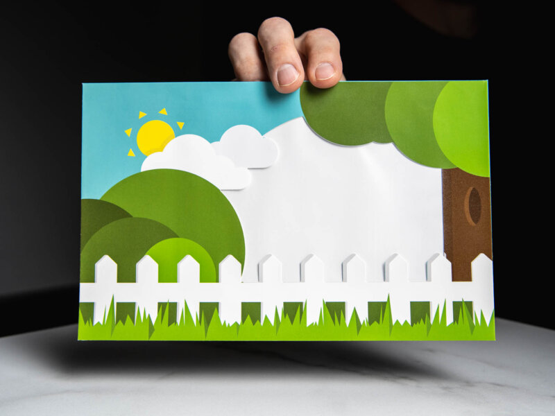 Envelope with trees, grass, a white fence, and the sun