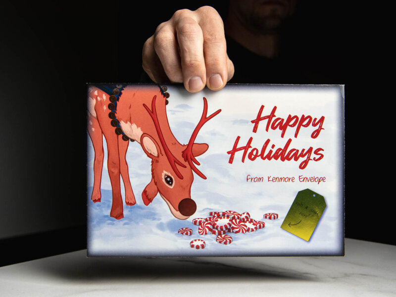 Hand holding envelope with Christmas reindeer and Happy Holidays from Kenmore Envelope on it